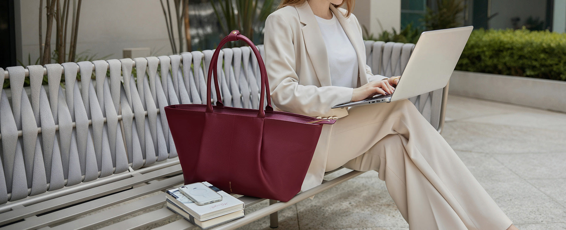 A woman working on a laptop with the Victoria Hyde London red Ada bag beside her — a stylish tote bag that combines modern design, practicality, and effortless elegance.