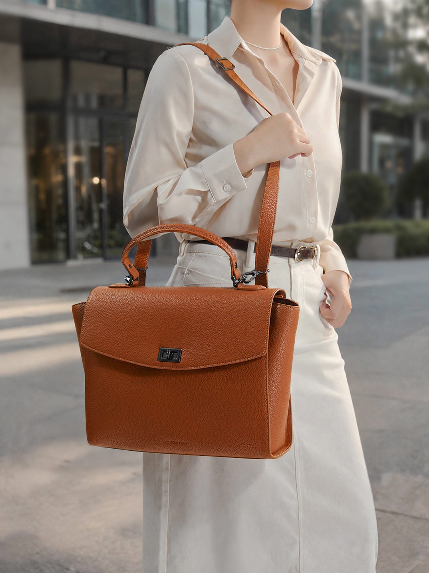 Model carrying the Victoria Hyde Potter 2-in-1 convertible laptop bag in brown as a shoulder bag, made of stylish, ergonomic vegan leather.