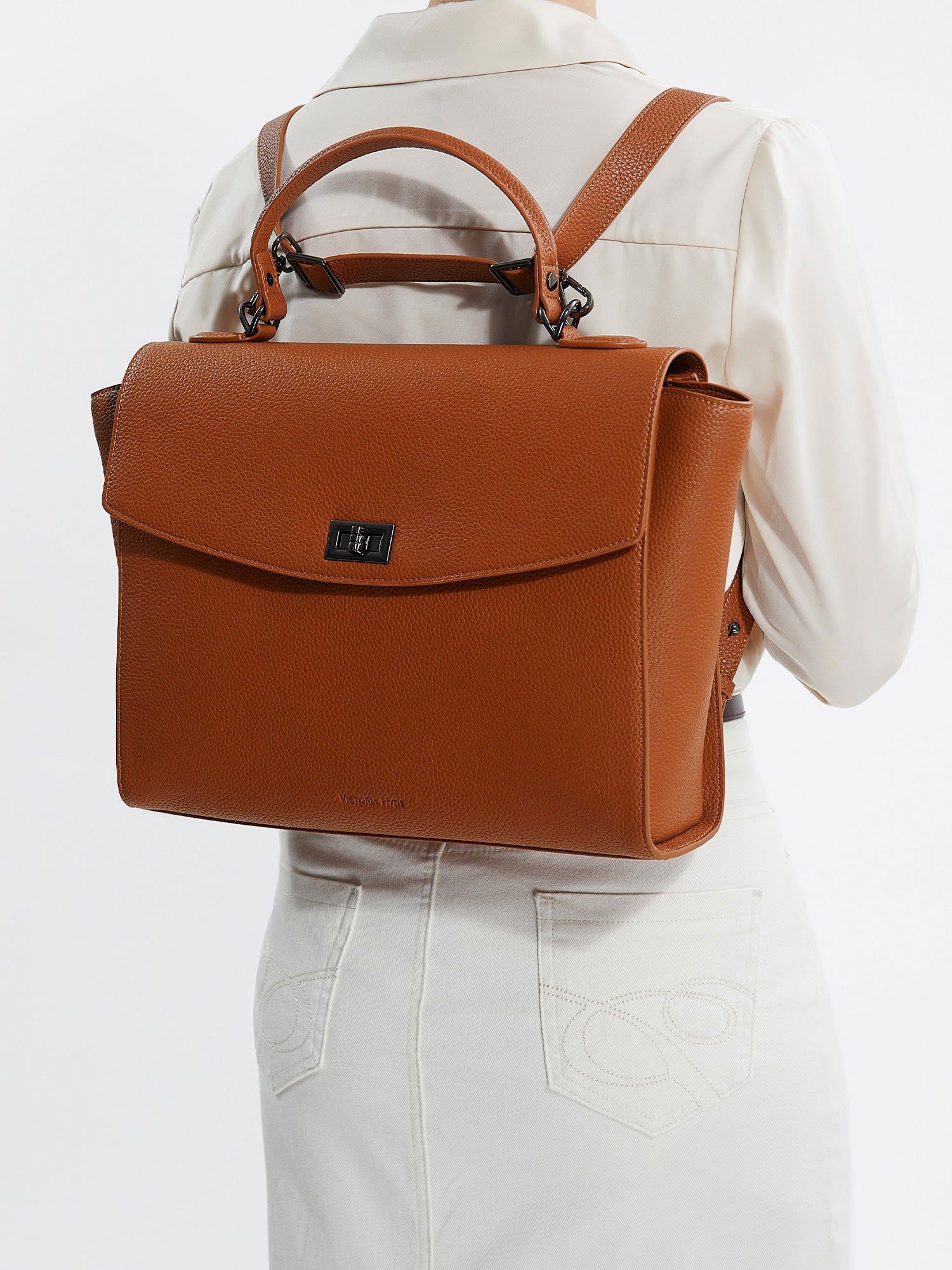 Model wearing Victoria Hyde Potter 2-in-1 brown laptop backpack, styled as a chic and ergonomic shoulder bag for professional commuters.